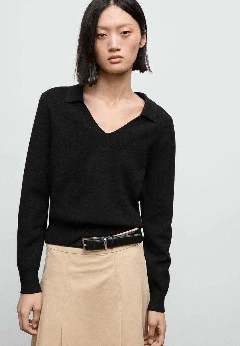Schwarzer V-Ausschnitt-Pullover mit langen Ärmel, gerippten Bündchen und glatter Textur. Kombiniert mit einem beigen Rock und einem schwarzen Gürtel.