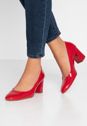 Chaussures à talons hauts en cuir verni rouge, avec un bout arrondi et un talon épais. Le design présente une surface lisse et brillante ainsi qu'une silhouette minimaliste.
