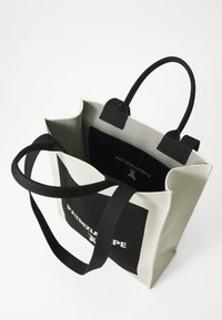 Borsa a tracolla con una combinazione di colori beige e nera, realizzata in tessutotexture. Dettagli notevoli includono due manici neri e stampa del logo all'interno.