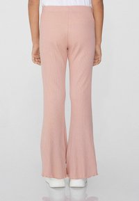 Helles rosa, gerippte, ausgestellte Hose mit einem rohem Saum, ausgestattet mit einer taillierten Taille und einer weichen Textur, kombiniert mit weißen Schuhen.