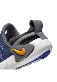Gros plan sur le talon d’une basket avec une languette grise, une empeigne grise et bleue, une semelle blanche et un logo swoosh jaune sur une pièce de support grise.