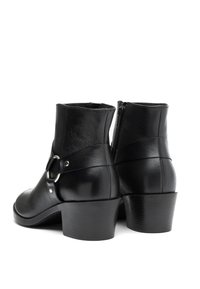 Bottines en cuir noir avec des talons bas en blocs, fermeture éclair sur le côté, et détail de sangle en anneau argenté, présentées de dos sur un fond blanc.