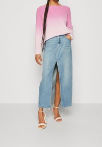 Lichtroze naar witte gradient geribbelde trui, gecombineerd met een lichtblauwe denimrok met hoge split. Geaccentueerd met witte sleehakken.