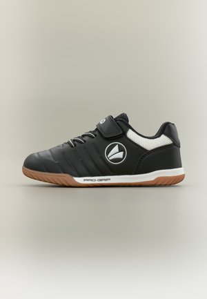 Zwart-witte sportschoen met gumzool, klittenbandsluiting, veters en een rond logo aan de zijkant, getoond in zij-aanzicht op een neutrale achtergrond.