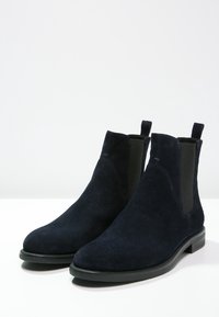 Botas Chelsea de ante azul marino con paneles laterales elásticos, puntera redondeada y suela de goma plana con sutilezas en los detalles de costura.