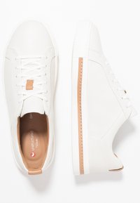 Weiße Leder-Sneaker mit glatter Oberfläche, ausgestattet mit beigen Akzenten an der Ferse und an der Seite, kontrastierenden Schnürsenkeln und einer strukturierten weißen Sohle.