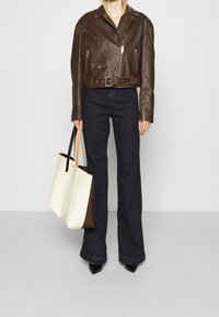 Brun lädercropjacka med bälte, tillsammans med mörkblå utsvängda jeans och en tvåfärgad toteväska i kräm och brunt.