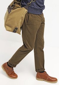 Hnědé chinos, tmavě modrá mikina, hnědé kožené boty. Nese světle hnědou messenger tašku s tmavě hnědými akcenty. Hladká textura, volný střih.