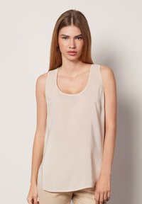 Beige ärmlös topp med rundad halsringning, tillverkad av mjukt tyg. Har en lätt drapering och är ärmlös med breda axelband.