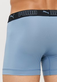 Világoskék boxer nadrág fekete derékkal, amelyen a Puma logo található. Sima anyag, oldalain texturált panellel.