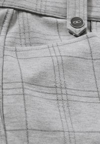 Grå rutigt tyg med en vävd struktur och synlig sömnad, en knappstängning och detalj av ficka i en närbild.