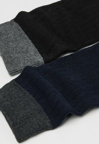 Dwie pary skarpetek z prążkowanego materiału: jedne czarne z szarym mankietem, a drugie granatowe z kontrastowym szarym mankietem. Teksturowana tkanina, casualowy design.