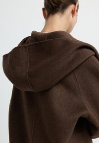 Brauner Woll-Hoodie mit großer Kapuze, weichem Textil und genähten Details auf der Rückseite. Einfaches und minimalistisches Design.