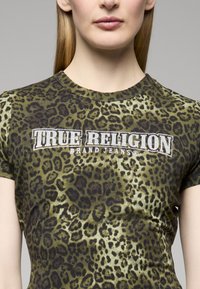 Tričko se vzorem leopardí kůže v zelené a černé barvě, s logem "True Religion" zdobeným kamínky. Krátké rukávy a kulatý výstřih.