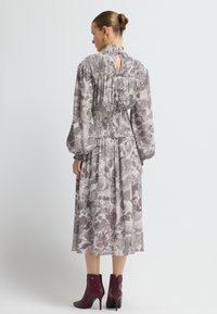 Vestido midi con estampado floral en tejido suave, con corsé fruncido y mangas abullonadas. Presenta un diseño de espalda con ojal y se combina con botas de tobillo burdeos.