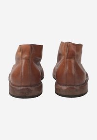 Bottines en cuir marron avec une finition lisse, bout rond et talon empilé. Couture visible le long des coutures arrière.