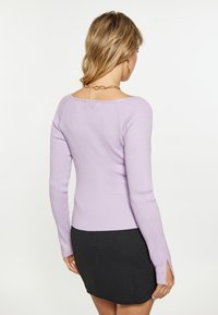 Lavendelfarbenes, geripptes Sweater mit langen Ärmeln und seitlichen Schlitzen, kombiniert mit einem schwarzen Rock. Glatte Textur, figurbetontes Design, keine sichtbaren Muster.