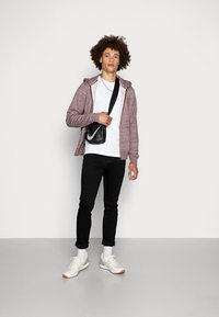 Un hoodie zippé bordeaux sur un T-shirt blanc, un jean slim noir, des baskets blanches avec des accents orange, et un sac bandoulière noir.