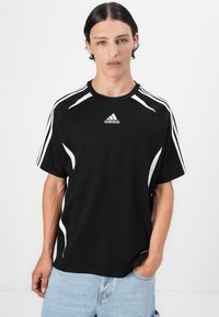 T-shirt de sport noir avec des accents blancs et trois bandes sur les épaules, doté d'un col rond et d'une texture de tissu douce.