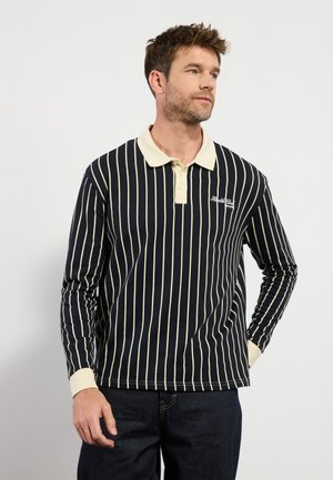 Camisa de polo de manga larga en azul marino con rayas verticales blancas. Cuenta con un cuello y puños beige, y un pequeño logo en el pecho.