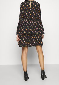 Svart klänning med blommönster i rosa, gult och grönt. Har långa ärmar, ett lager på lager-skirt och nyckelhålsdetalj i ryggen.