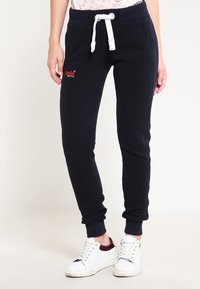 Marinblå joggers med dragsko i midjan och vita detaljer, med två sidofickor och ett mjukt, texturerat tyg.