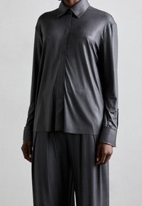 Mörkgrå sidentopp med lång ärm och krage, framknäppning och lös passform. Slät textur och subtil glans synlig.