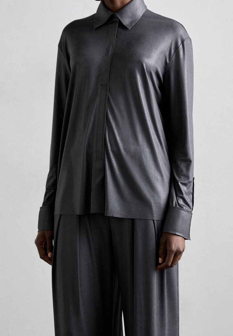 Mörkgrå sidentopp med lång ärm och krage, framknäppning och lös passform. Slät textur och subtil glans synlig.