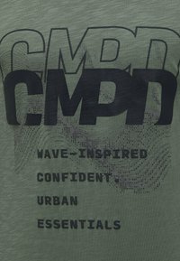 Green fabric with layered black text "C.M.P.A" and phrases "Wave-inspired," "Confident," "Urban," and "Essentials" with wave-like graphic lines.