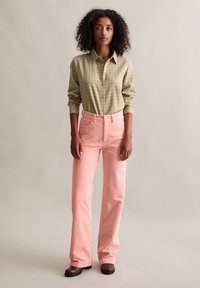 Zielona koszula w kratę na guziki zestawiona z jasnoróżowymi sztruksowymi spodniami z wysokim stanem, o prostych nogawkach, oraz prostymi brązowymi butami.