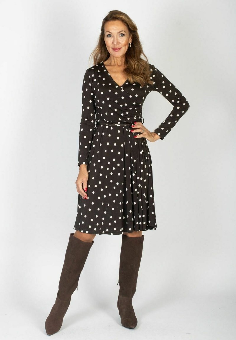 Czarna sukienka w białe kropki z długimi rękawami, zapinana na krzyż, z plisowanym dołem i wiązaniem w talii. Zestawiona z brązowymi zamszowymi kozakami do kolan.