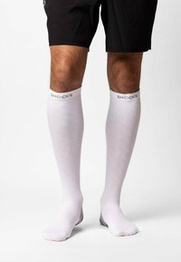 Calze bianche fino al ginocchio con un design testurizzato, dotate di un bordo grigio nella parte superiore con la scritta "SNOCKS" stampata in bianco.