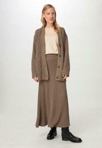 Brauner gerippter Strickcardigan mit langen Ärmeln, großen Knöpfen und Taschen, kombiniert mit einem passenden gerippten Maxirock und einem beigen Oberteil.