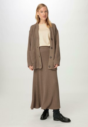 Cardigan en tricot côtelé marron avec des manches longues, de gros boutons et des poches, associé à une jupe maxi côtelée assortie et un haut beige.