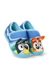 Zapatos azul claro para niños que se deslizan, con caras de perro de dibujos animados en la puntera; uno negro y amarillo, el otro naranja y blanco.