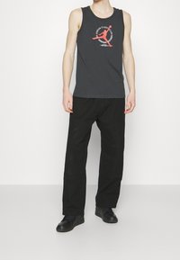 Grå ärmlös linne med en grafisk logotyp i rött i mitten, ihopparat med svarta byxor och svarta skor. Enkelt, avslappnat stilig.