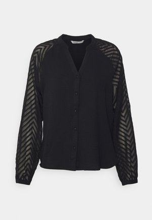 Schwarze Bluse mit Knopfleiste, durchsichtigen langen Ärmeln mit Chevron-Muster und einem Oberkörper aus festem Stoff.