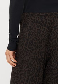 Pantaloni a stampa leopardo in tessuto marrone scuro con una vita elastica nera. Presentano una texture liscia e una vestibilità comoda.