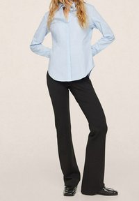 Chemise bleu clair à manches longues avec col et boutons, associée à un pantalon évasé noir et des chaussures habillées noires, mettant en valeur une coupe décontractée.