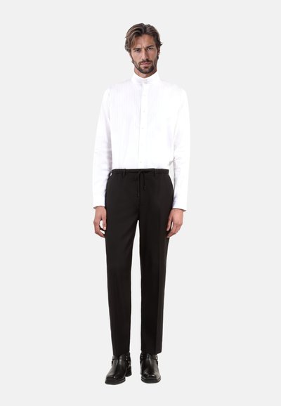 Witte button-up shirt met verticale strepen, gecombineerd met zwarte taps toelopende broek met een trekkoord in de taille. Zwarte leren enkelboots.