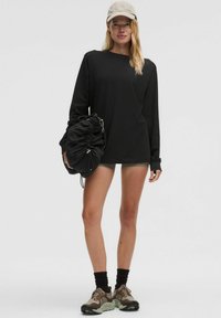 Chemise noire à manches longues, casquette beige, avec un sac noir doux et un short. Les chaussures présentent des accents gris et vert olive ; design pratique et sportif.