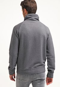 Harmaa college-pusero korkealla kauluksella, ribbaillut hihat ja helma, sileä pinta ja raglan-hihat, nähtynä takaa.