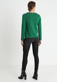 Maglione verde lavorato a maglia con scollo tondo, abbinato a jeans neri skinny e stivaletti neri con tacco, visto da dietro.