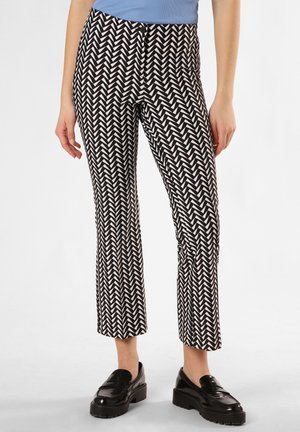 Schwarz-weiße Herringbone-Musterhosen mit schlanker Passform, knöchellang und glatter Textur, kombiniert mit glänzenden schwarzen Loafers.