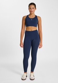 Reggiseno sportivo e leggings blu navy realizzati in tessuto elasticizzato. Entrambi presentano una texture liscia e un design aderente. Decorati con un piccolo logo.