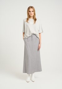 Szürke, oversized póló logóval, amelyhez egy magas derekú, hosszú szürke szoknya tartozik. A modellen fehér bokapercsizmák vannak. Egyszerű, minimalista kialakítás.