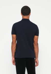 Marineblå polo-skjorte med korte ermer og klassisk krage, laget av et glatthåndtert stoff, har rett snitt og subtile sømdetaljer.