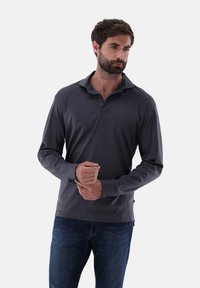 Graues Langarm-Polohemd mit Kragen, vier Knöpfen und elastischen Bündchen. Getragen mit blauen Jeans, aus einem glatten, leichten Stoff.