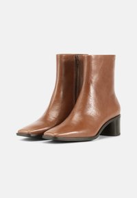 Ruskeat nahkaiset nilkkurit, joissa on terävä kärki, sivuvetoketju ja paksu korko. Sileä pinta kiiltävällä viimeistelyllä.