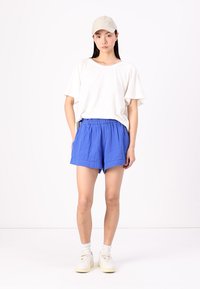 Hvit t-skjorte med korte ermer kombinert med blå linshorts, som har elastisk midjebånd og en avslappet passform, båret med hvite joggesko.